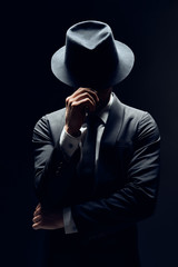 Fototapeta Man in suit hiding face behind his hat isolated on dark background obraz