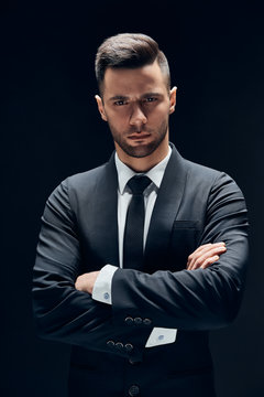 Handsome confident man in black suit with arms crossed on dark background