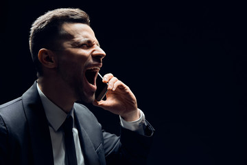 Man screaming talking on mobile phone with copy space isolated on dark background