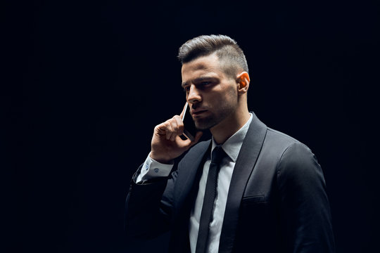 Handsome man in suit talking on mobile phone isolated on dark background