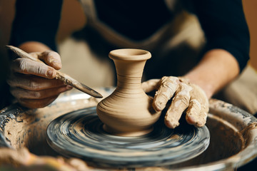 Man potter working on potters wheel making ceramic pot from clay in pottery workshop - obrazy, fototapety, plakaty