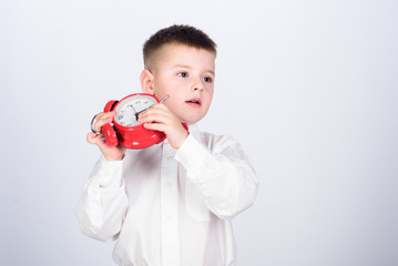 Morning routine. Schoolboy with alarm clock. Kid adorable boy white shirt red bow tie. Develop self discipline. Set up alarm clock. Child little boy hold red clock. It is time. Schedule and timing