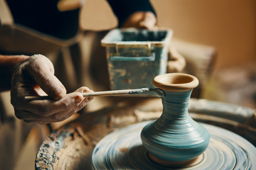 Man painting handmade pottery at ceramic workshop - obrazy, fototapety, plakaty