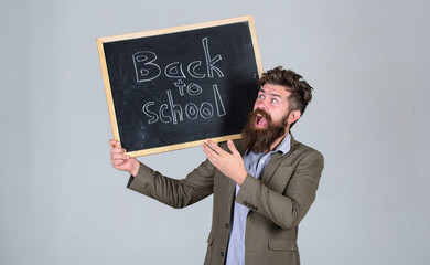 Prepare for new school year. Teacher bearded man stands and holds blackboard inscription back to school grey background. Teacher advertises back to studying, begin school year. Are you ready to study