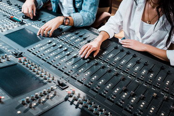 cropped view of two multicultural sound producers working at mixing console in recording studio