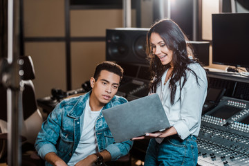 beautiful sound producer using laptop near mixed race friend in recording studio