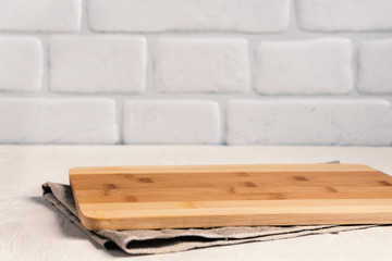 Obraz na płótnie Canvas Background kitchen with cutting board on white wooden table, with linen tablecloth against the background a brick wall.