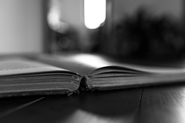 Old, aged opened book on wooden floor, entering light from the window in black and white.