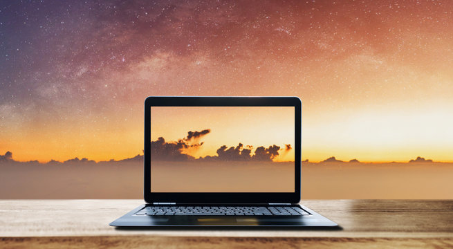 Computer laptop on wooden desk and sunrise sky with stars background
