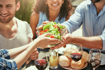 Enjoying picnic together. Cropped image of woman giving fresh salad to her friend while having summer picnic outdoors