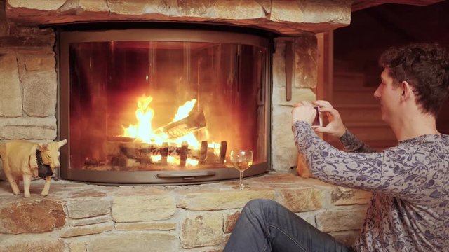 Man Takes a Photo of the Cozy Fire with His Smartphone.