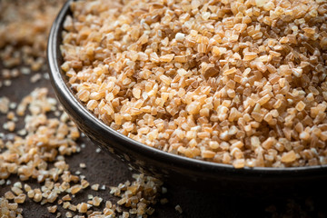 Dry crushed spelt in a bowl on a dark background.