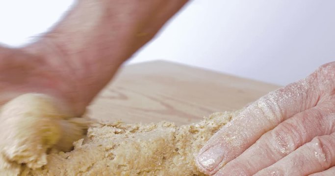 Mani di un uomo che impastano la pasta per la pizza fatta in casa con farina acqua sale e lievito su un tagliere di legno in cucina.