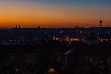 Fototapeta na wymiar Prague, capital city of the Czech Republic, at dawn, silhouette of Zizkov tower on horizon, red, yellow, blue and orange sky, urban landscape with houses in shadow, panoramic view