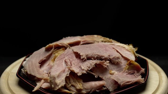 Easter cooked ham sliced on a plate; rotating on a turntable; isolated on a black background.