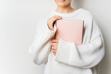 Close view of woman in white woolen sweater holding a book with empty pink cover in hands. Free...