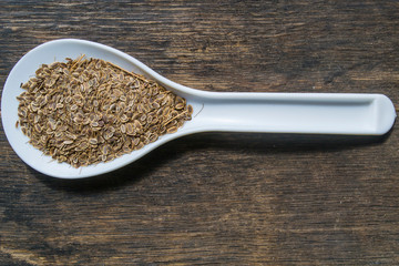 Dill seeds in a spoon on a wooden table.