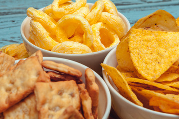 Salty snacks. Pretzels, chips, crackers on wooden background. Unhealthy products