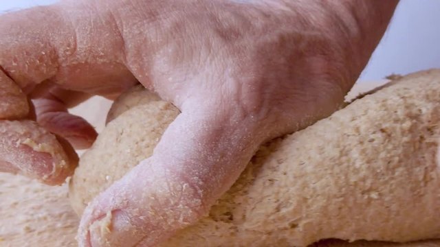 Mani di un uomo che impastano la pasta per la pizza fatta in casa con farina acqua sale e lievito su un tagliere di legno in cucina.