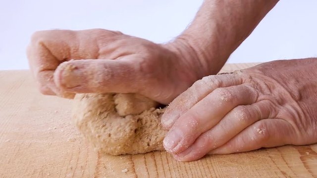 Mani di un uomo che impastano la pasta per la pizza fatta in casa con farina acqua sale e lievito su un tagliere di legno in cucina.