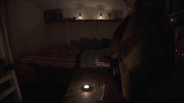 Woman pouring two glasses of wine in a small and cozy candle lit cabin at night time