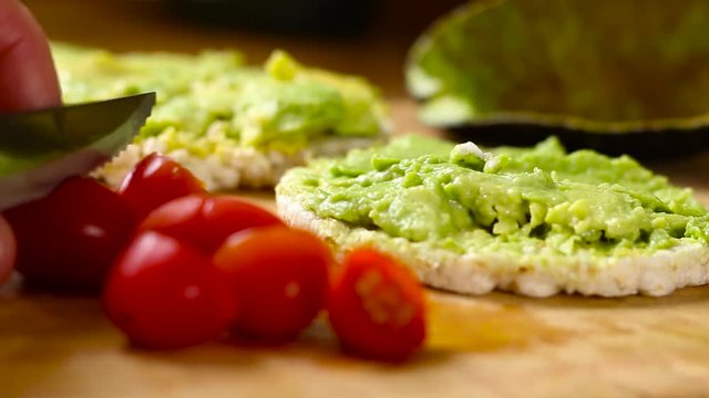 Preparation of fresh tomatoes and avocado spread on rice crackers on wooden chopping board