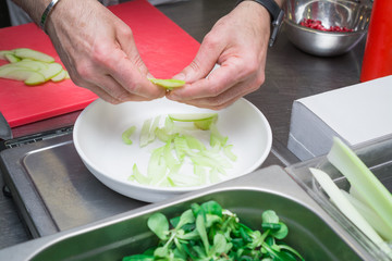 Cooks hands gently place a green apple on the plate, preparing a delicious salad in the kitchen