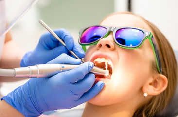 Preteen girl receiving teeth cleaning procedure in pediatric dental clinic