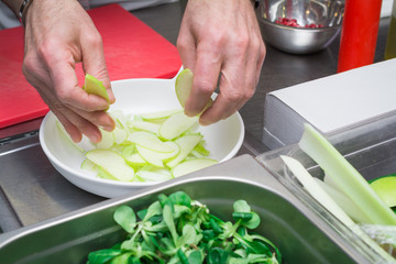 Cooks hands gently place a green apple on the plate, preparing a delicious salad in the kitchen