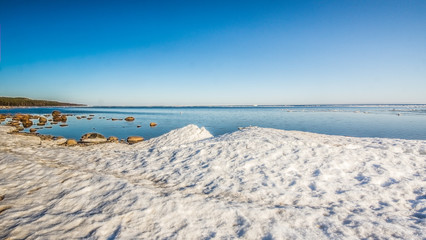 Snow pile, hill. Large snow drift isolated on a blue sky background,  outdoor view of ice blocks at frozen finland lake in winter