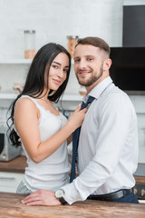 cheerful brunette girl touching tie of happy bearded boyfriend in suit