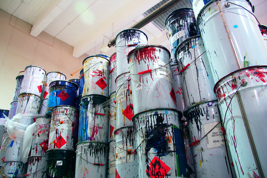A collection of paint cans, glue buckets, mastic and toxic and hazardous material stacked