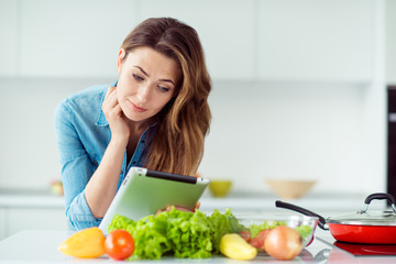 Close-up portrait of her she nice lovely attractive concentrated smart brown-haired lady reading online literature cookery gastronomy meal dinner lunch delicacy in light white interior style kitchen