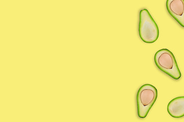 Scattered halves with and without kernels of organic avocado on yellow table in kitchen or market. Top view. Cooking concept. Copy space for your text