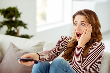 Fototapeta premium Close up photo of anxious nice attractive lady impressed by horror serials scream shout touch cheek student long curly wavy hair sit divan in modern apartment