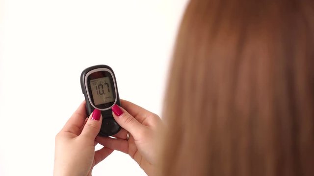 Close-up of the girl holding a glucometer in her hands and checking the blood sugar level, she presses the button and looks at the latest values in the glucometer. High blood glucose levels. 4K.