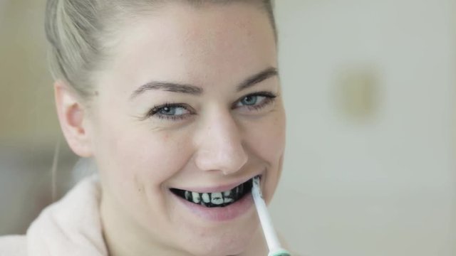 A Young Pretty Woman Smiles As She Brushes Her Teeth With Activated Charcoal For Teeth Whitening