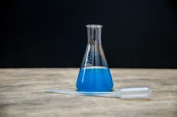 Chemical flask with blue laboratory dyes inside on a black background. The concept of expertise and medicine.