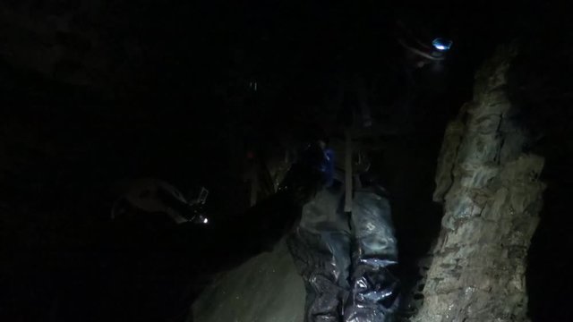 Cavers work themselves and their gear down an underground waterfall