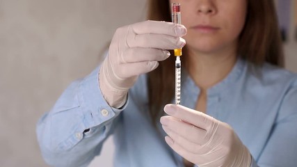 Close-up of a nurse in gloves and a uniform is typing a medicine in an insulin syringe. Vaccination, medicine, medicine. Slow motion. Close-up of a woman picking up insulin in an insulin syringe. - Powered by Adobe