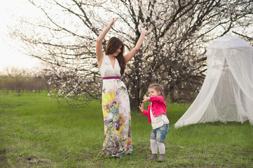 Naklejka na ściany i meble Beautiful young mother dancing and spinning with her daughter in forest glade. Happy family relationships. woman with baby playing outdoor. Maternal love, caring. Sunshine. Mother's Day