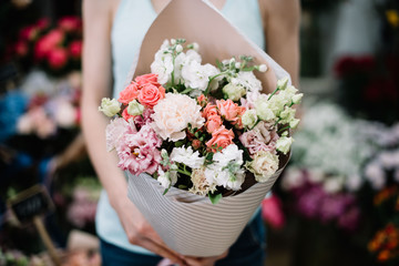 Very nice young woman holding beautiful blossoming flower bouquet of fresh eustoma, roses, matthiola, carnations in pastel colors on the flower stalls background at the florist shop
