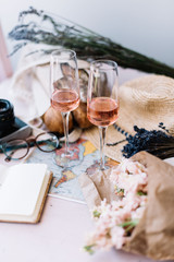 Fototapeta na wymiar summer travel set: two glasses of rose wine, paper notepad, beach hat, pastel cream coloured mattiola mono bouquet, fresh french lavender, vintage film camera, croissant and a bag of fresh baguettes