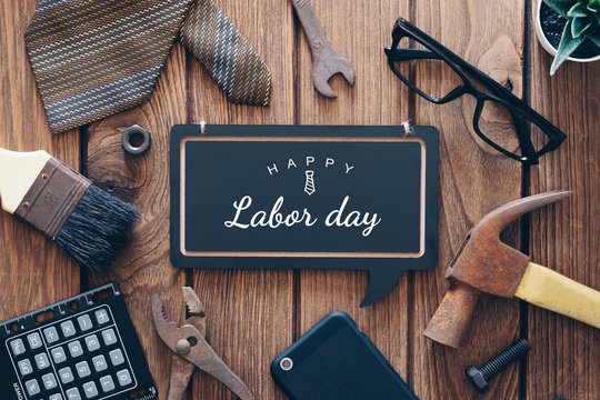 Happy Labor day background concept. Flat lay of construction blue collar handy tools and white collar's accessories over wooden background with text Happy Labor day on black chalkboard.