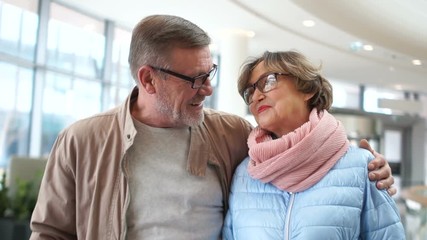A loving mature couple at the airport waiting for their flight. Laugh and talk, a woman lays a man's head on his shoulder - Powered by Adobe
