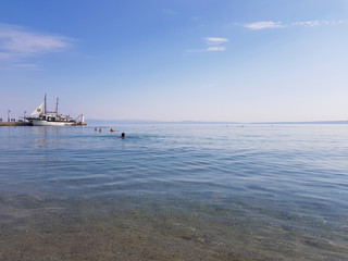 Calm sea in the morning with boat on the harbour and people swimming.