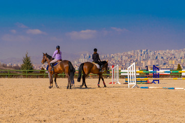 Two female friends horseback standing and horses relaxing and city view in background, Ankara, Turkey