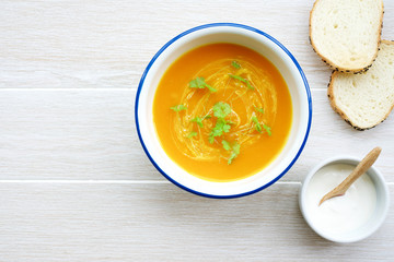 Pumpkin soup in white bowl with cream and parsley. Light wooden background