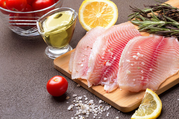 Tilapia fillet with lemon, rosemary and lettuce on a cutting board.