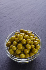 canned green peas in a glass bowl on a dark stone background